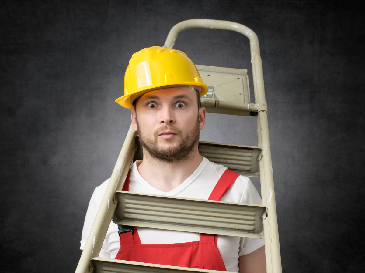 a man in a yellow helmet and red vest is sitting on a ladder